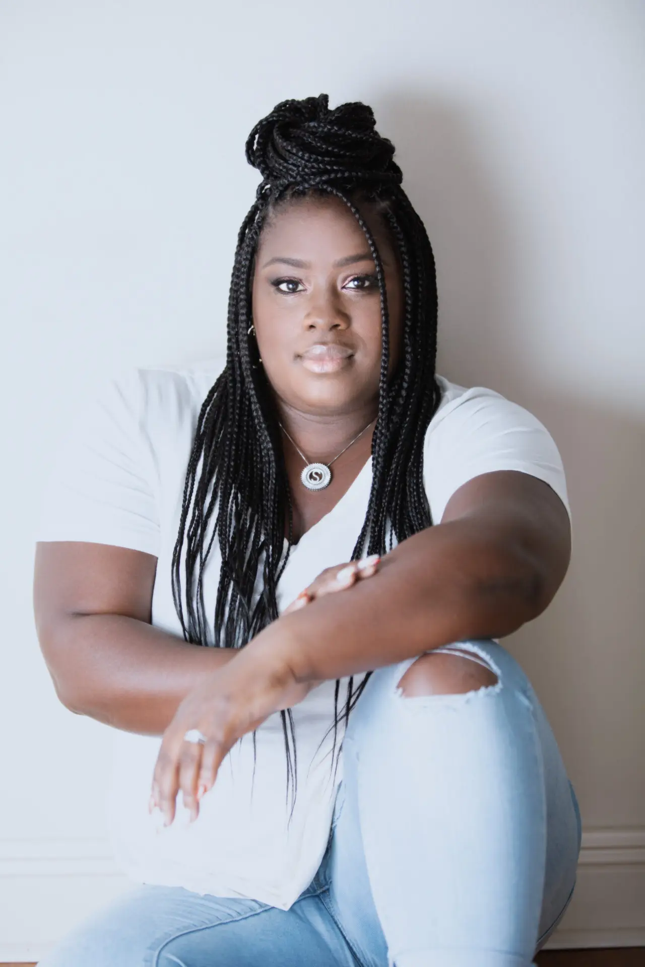 Portrait of a woman with long braids in a white top, seated, by Bellus Photography