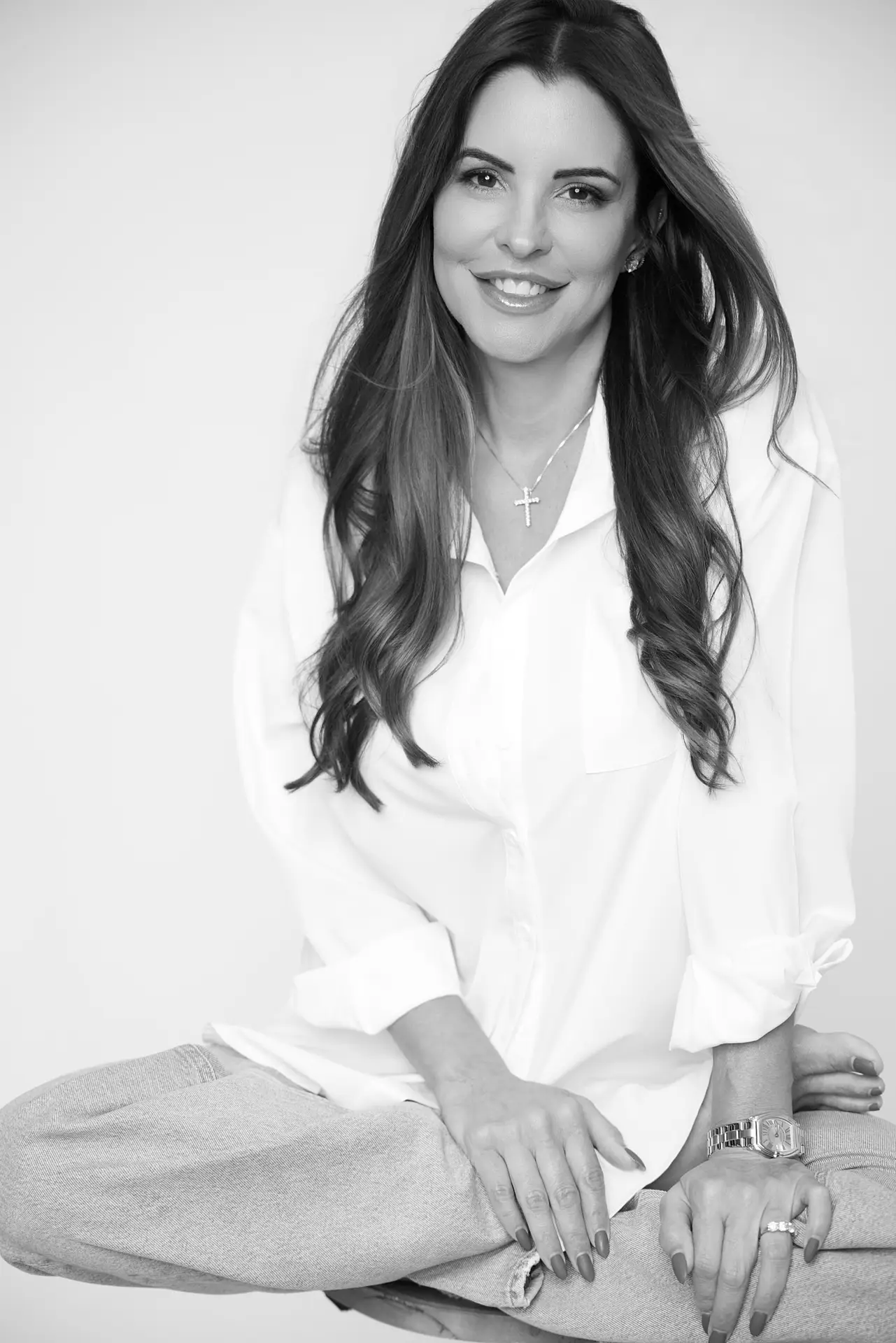 beautiful woman dressed in white button up shirt with blue jeans seated on studio floor