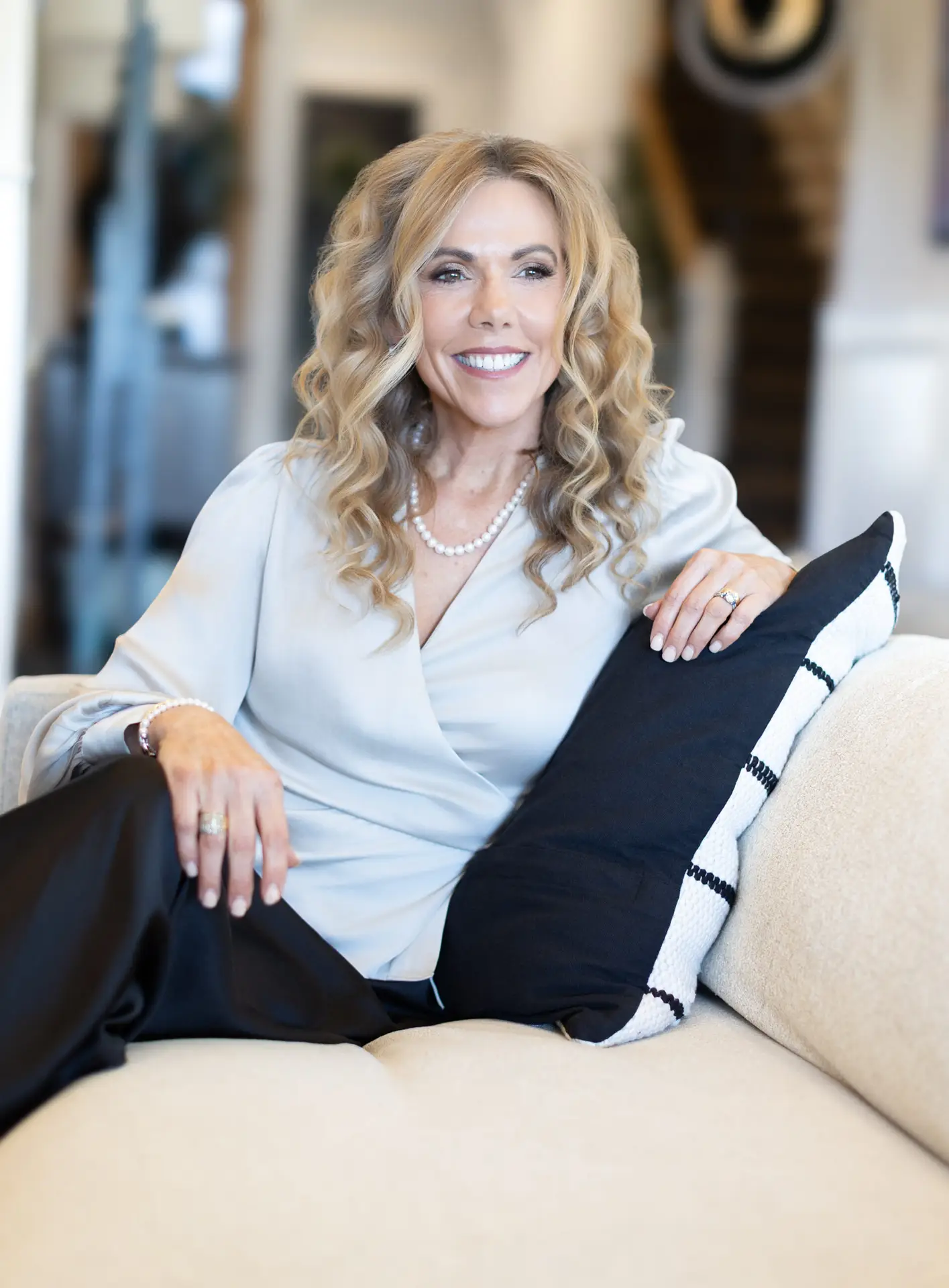 Personal branding portrait of a smiling woman with curly blonde hair seated on a cream sofa