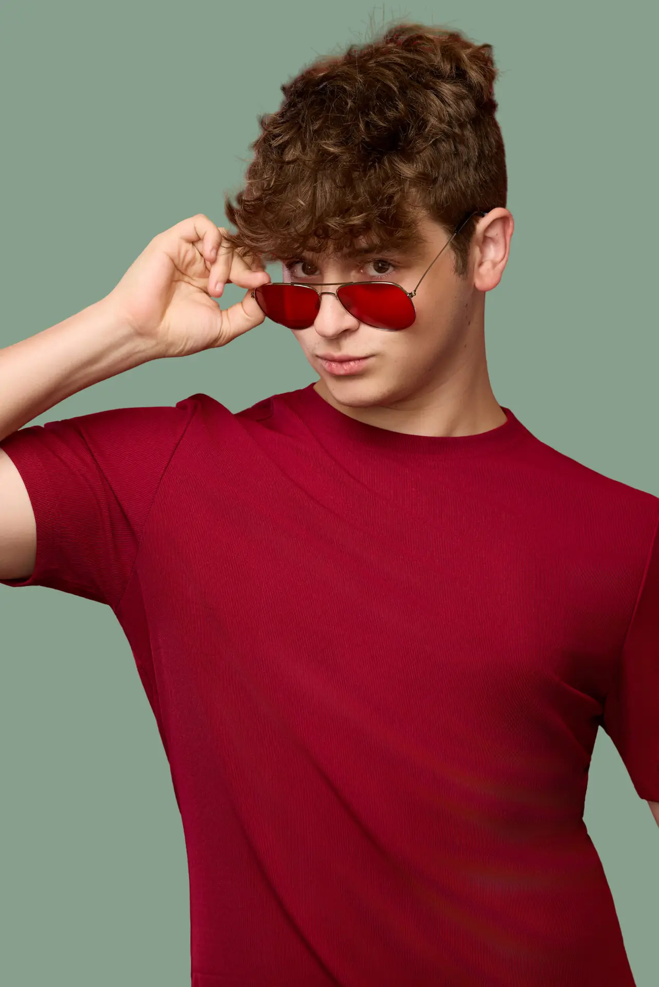 Studio portrait of a young man with curly hair lowering red sunglasses, by Bellus Photography